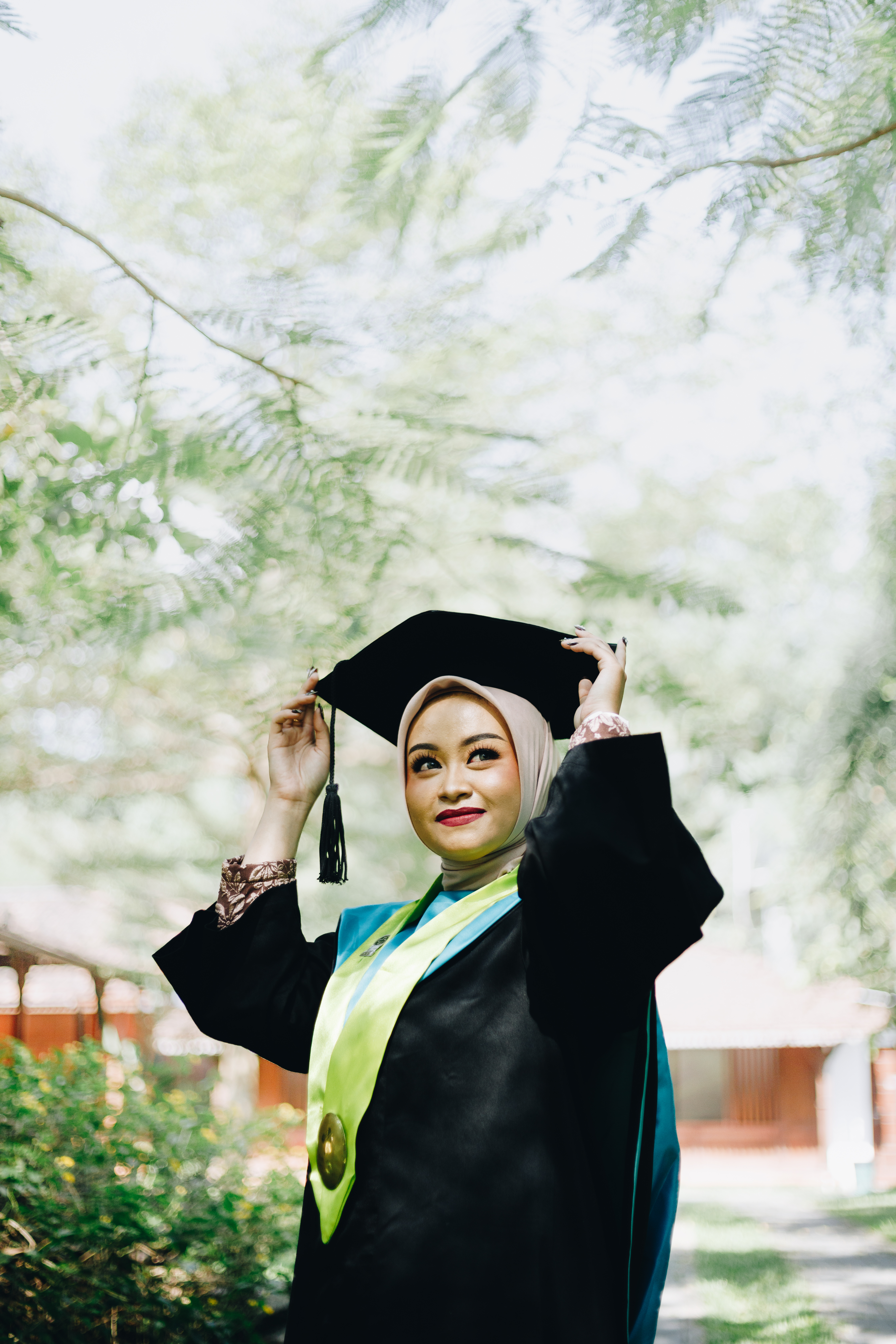 Foto wisuda outdoor mahasiswi UGM dengan toga hitam dan samir kuning di bawah sinar matahari hangat Bulaksumur Yogyakarta - Toga & Co.
