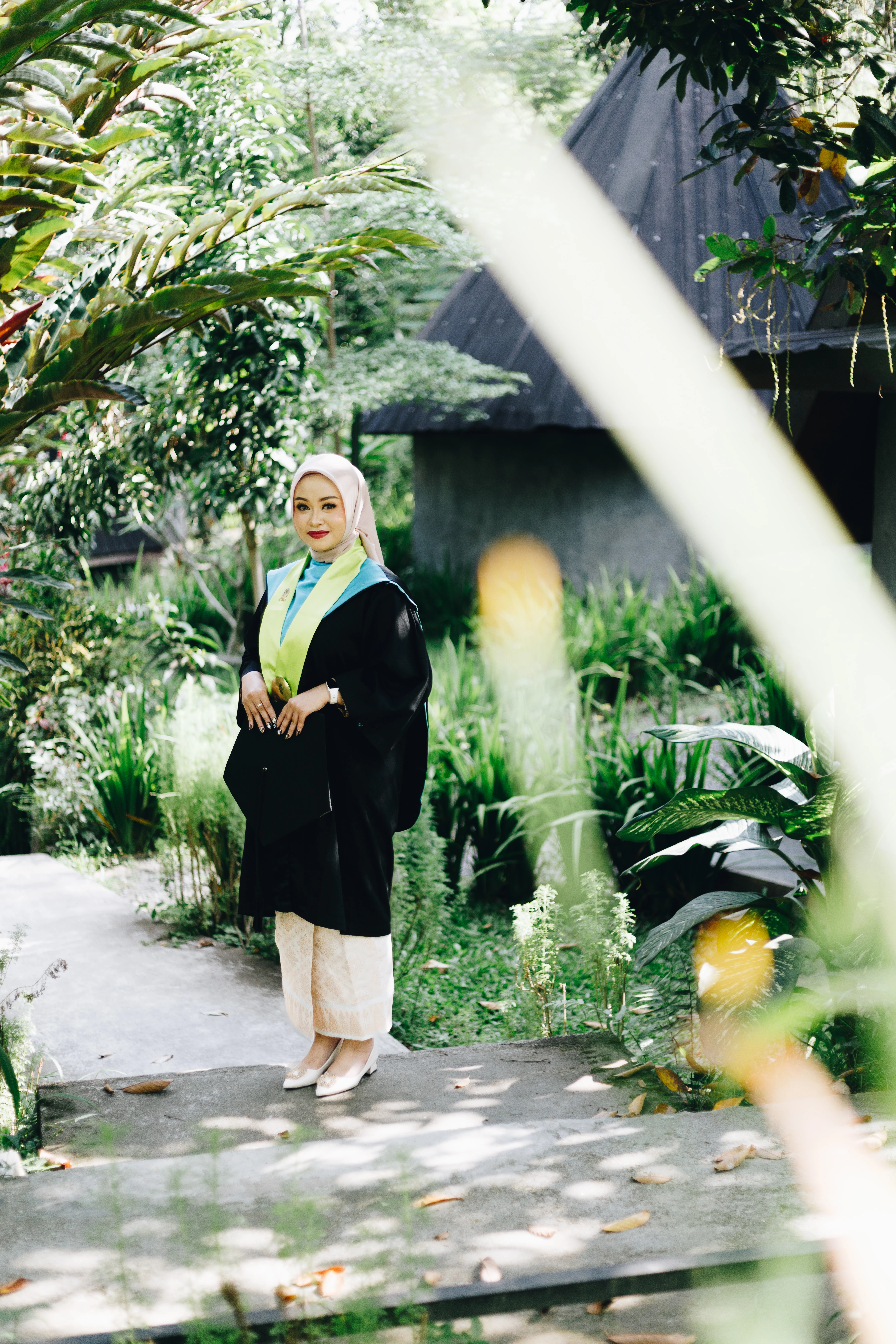 Foto wisudawati anggun berdiri di selasar Balairung UGM dengan pencahayaan natural lembut khas fotografi potret berkelas - Toga & Co.