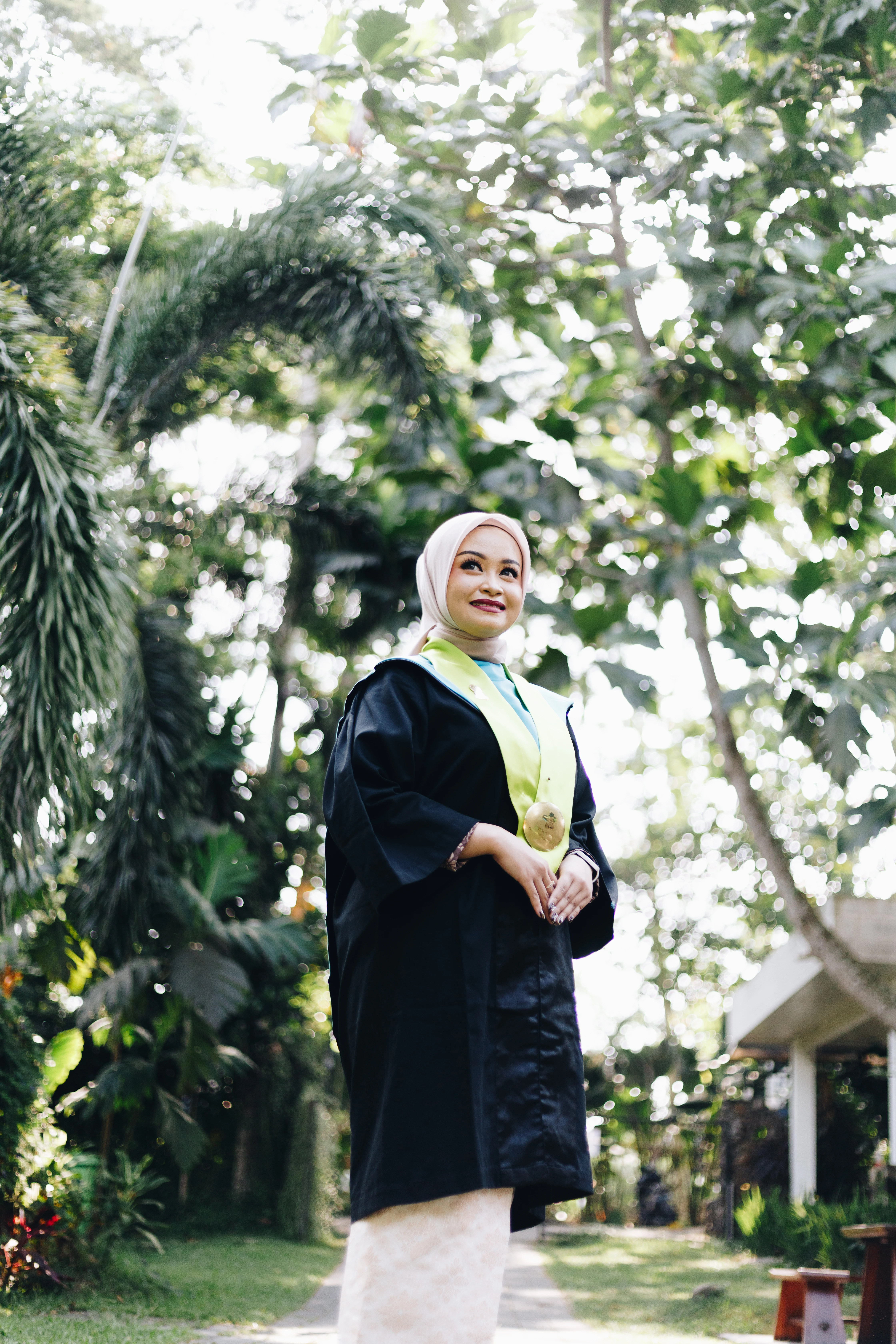 Foto potret wisuda wanita berhijab dengan toga dan kalung medali wisuda di tepi danau Lembah UGM - Toga & Co.
